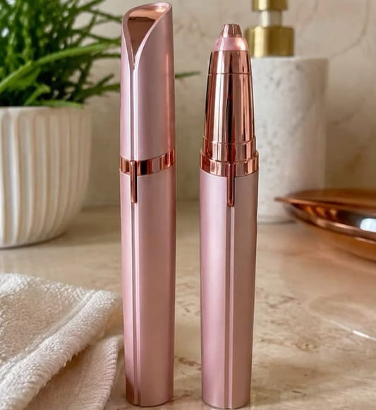 Two rose gold handheld beauty devices, likely facial hair removal or grooming tools, standing upright on a marble countertop with a towel and bathroom accessories in the background.
